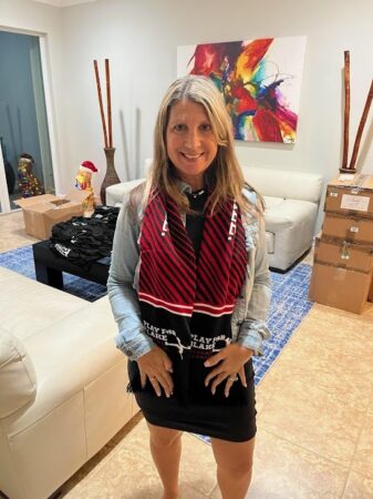Photo of a woman wearing a knit "Play for Blake" scarf in her living room.
